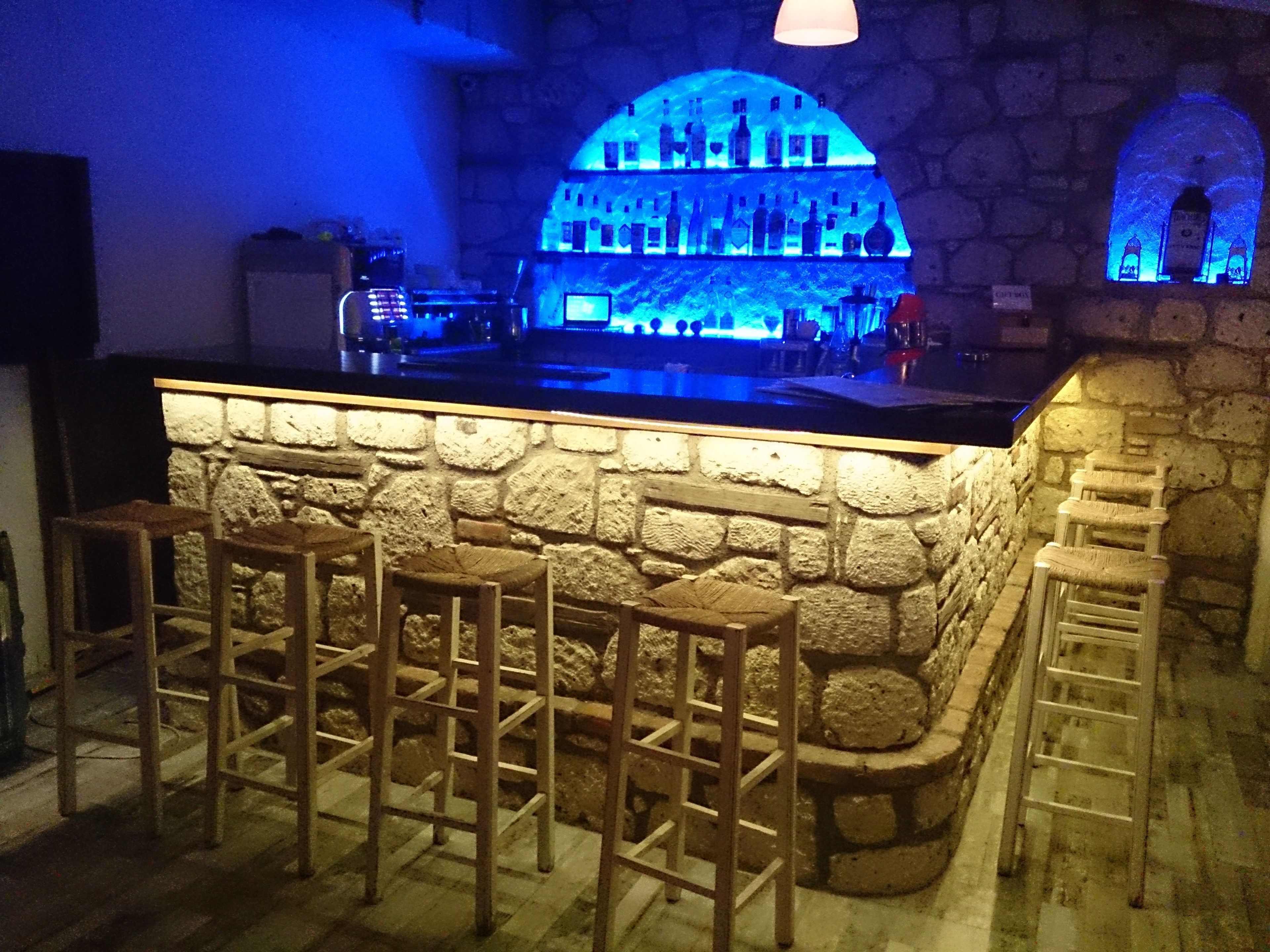 A bar area with stone walls, wooden stools, and a counter with bottles.