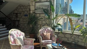 A sunlit room with stone walls, a staircase, and a view of a cityscape through large windows. - Imren Han Hotel - Special Class (Cesme)