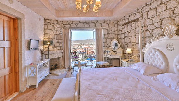 A bedroom with a stone wall, a bed with white bedding, a chandelier, and a view through a window. - Imren Han Hotel - Special Class (Cesme)