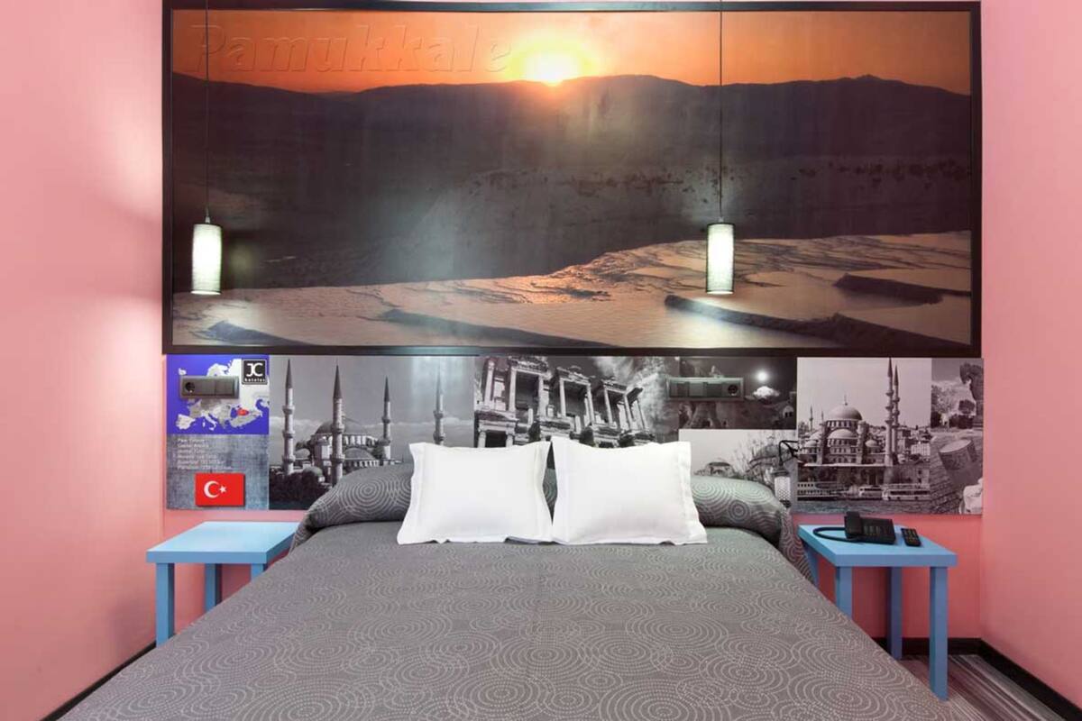 Un dormitorio con una cama, dos mesitas de noche, una lámpara de pared y un cuadro grande enmarcados sobre la cama.