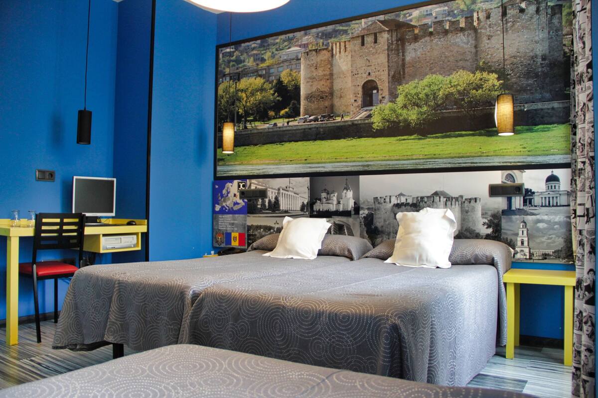 Habitación de hotel con una cama grande, un escritorio con computadora y televisor mostrando una vista panorámica.