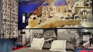 A bedroom with a bed, pillows, a red nightstand, a wall with photos, and a large poster of a coastal town. - Jc Rooms Santo Domingo (Madrid)
