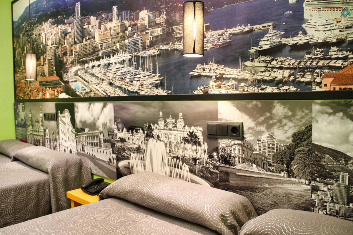 Habitación de hotel con un gran mural de la ciudad, una cama con ropa de cama estampada y una mesita con un teléfono.