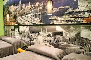 A hotel room with a large cityscape mural, a bed with patterned bedding, and a small table with a telephone. - Jc Rooms Santo Domingo (Madrid)