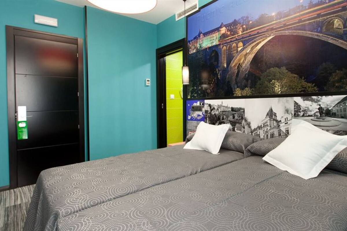 Una habitación de hotel con una cama, una mesita de noche, una pared con un mural de paisaje urbano y una puerta.