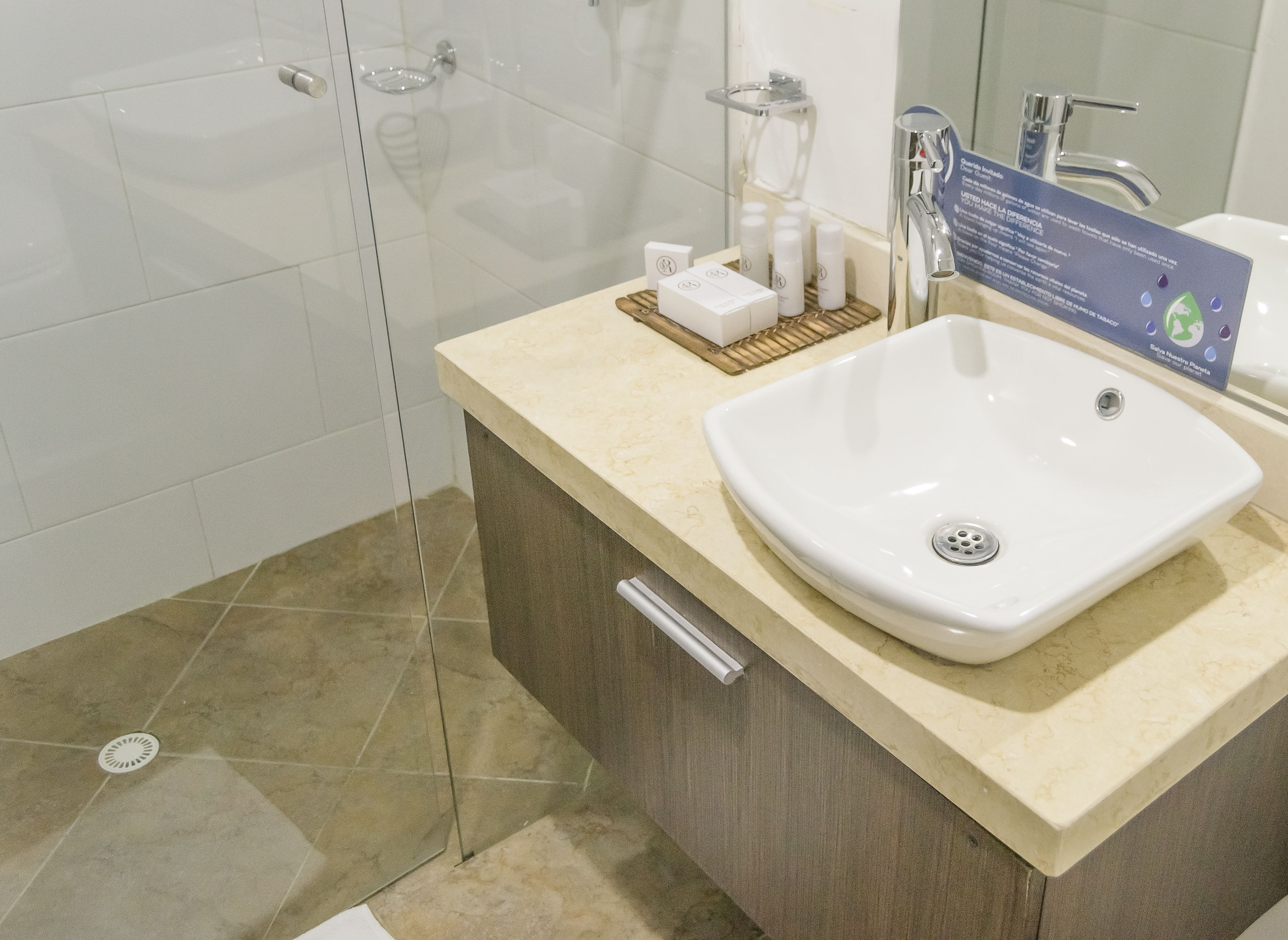 Un baño moderno con un lavamanos grande de color blanco, una cabina de ducha de vidrio y una encimera color beige.