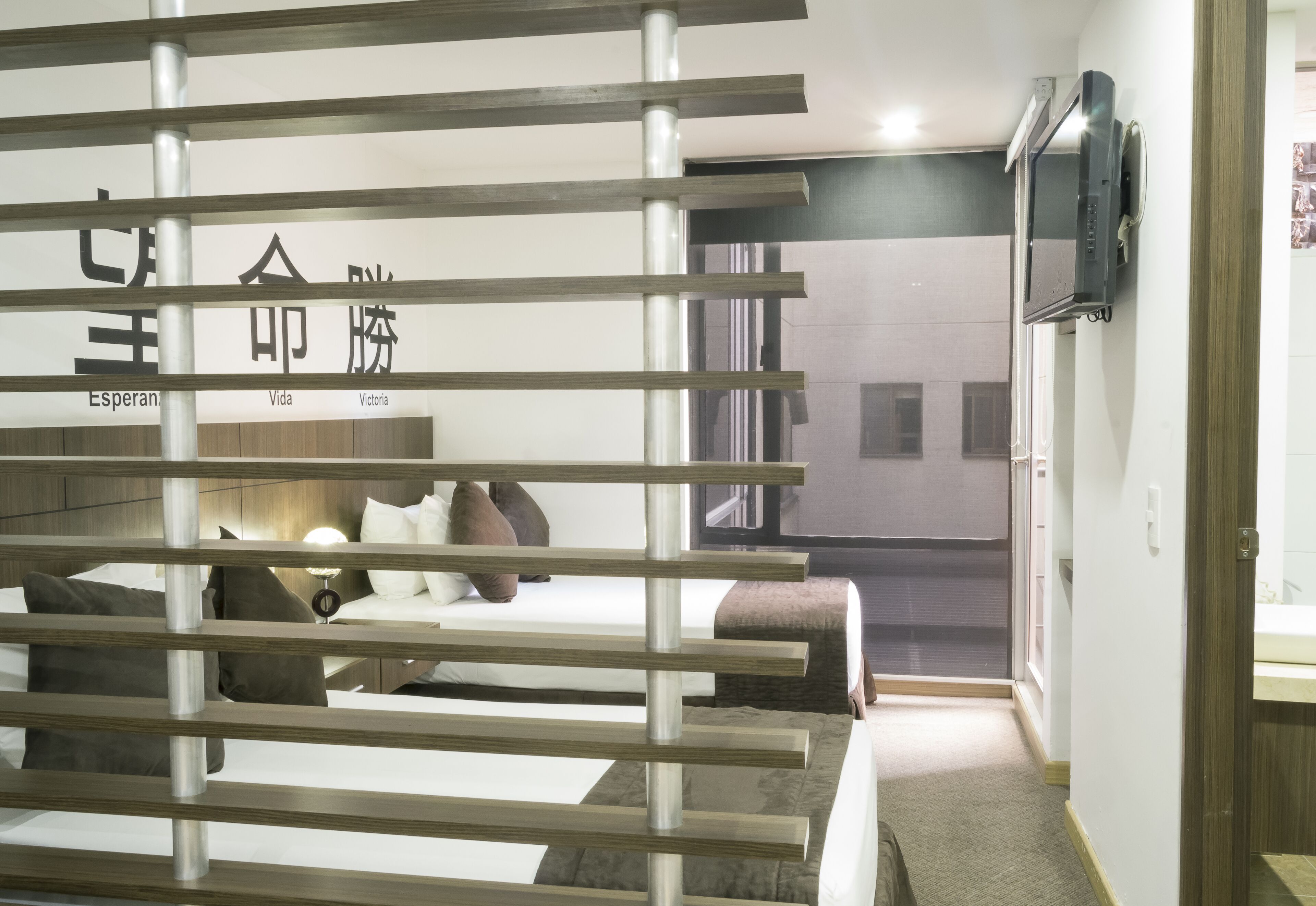 Habitación de hotel con una cama, un televisor montado en la pared y un cartel con texto.