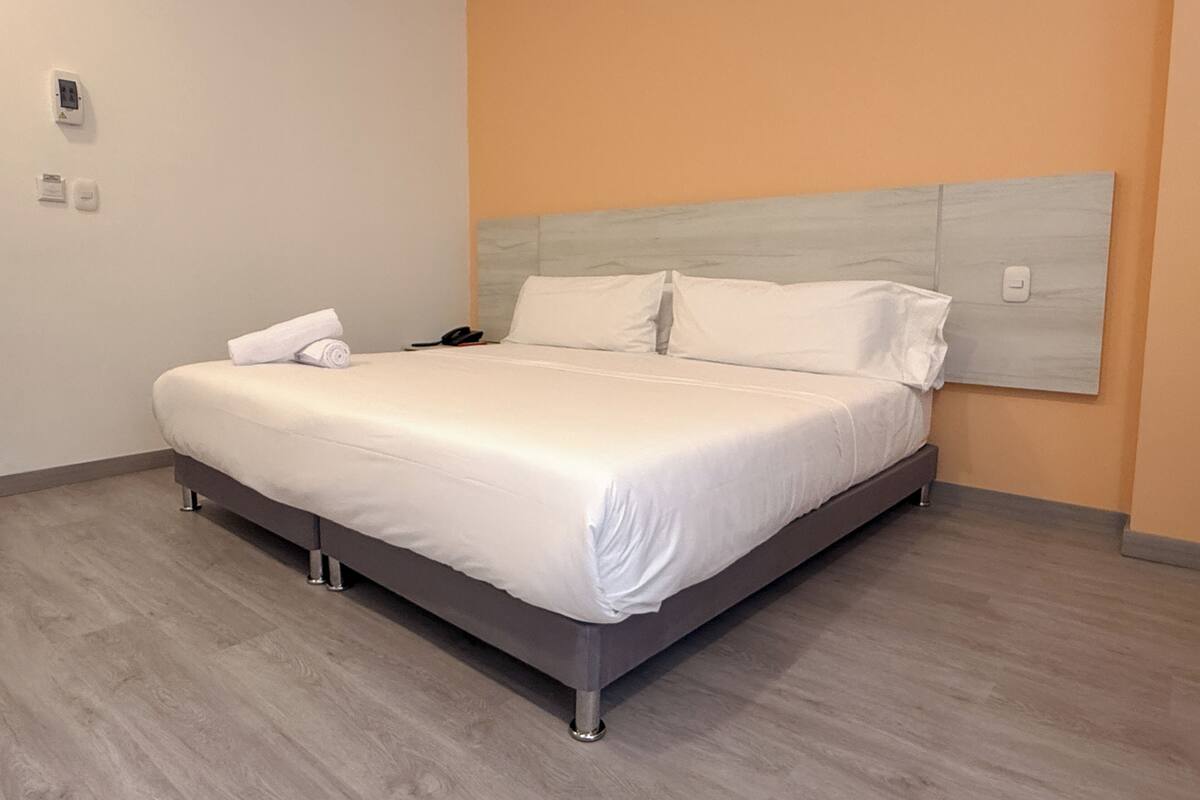 A modern hotel room with a large bed, a headboard, and a wooden floor.
