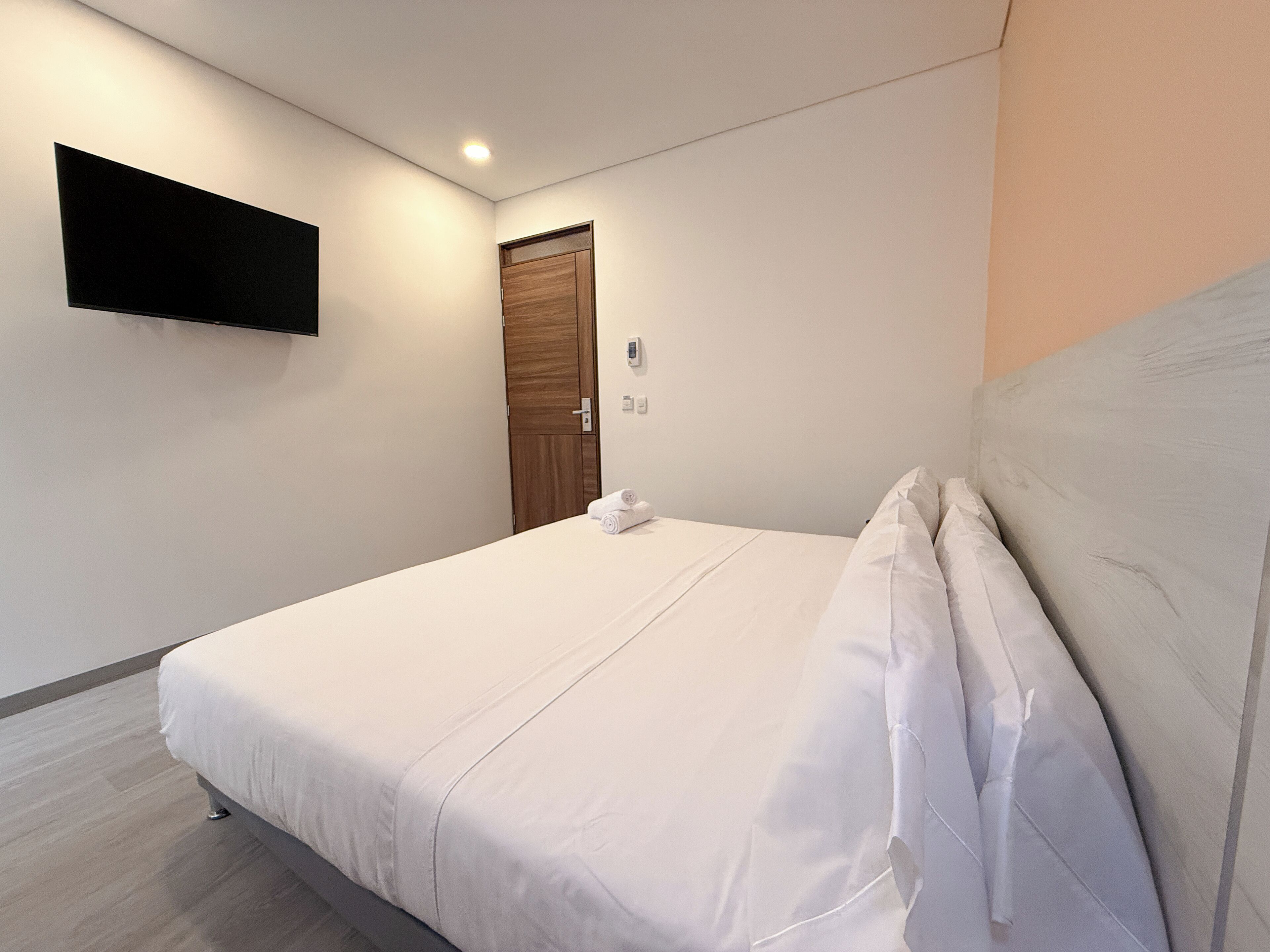 Un lit bien fait, avec du linge de lit blanc, un téléviseur à écran plat fixé au mur et une porte en bois.