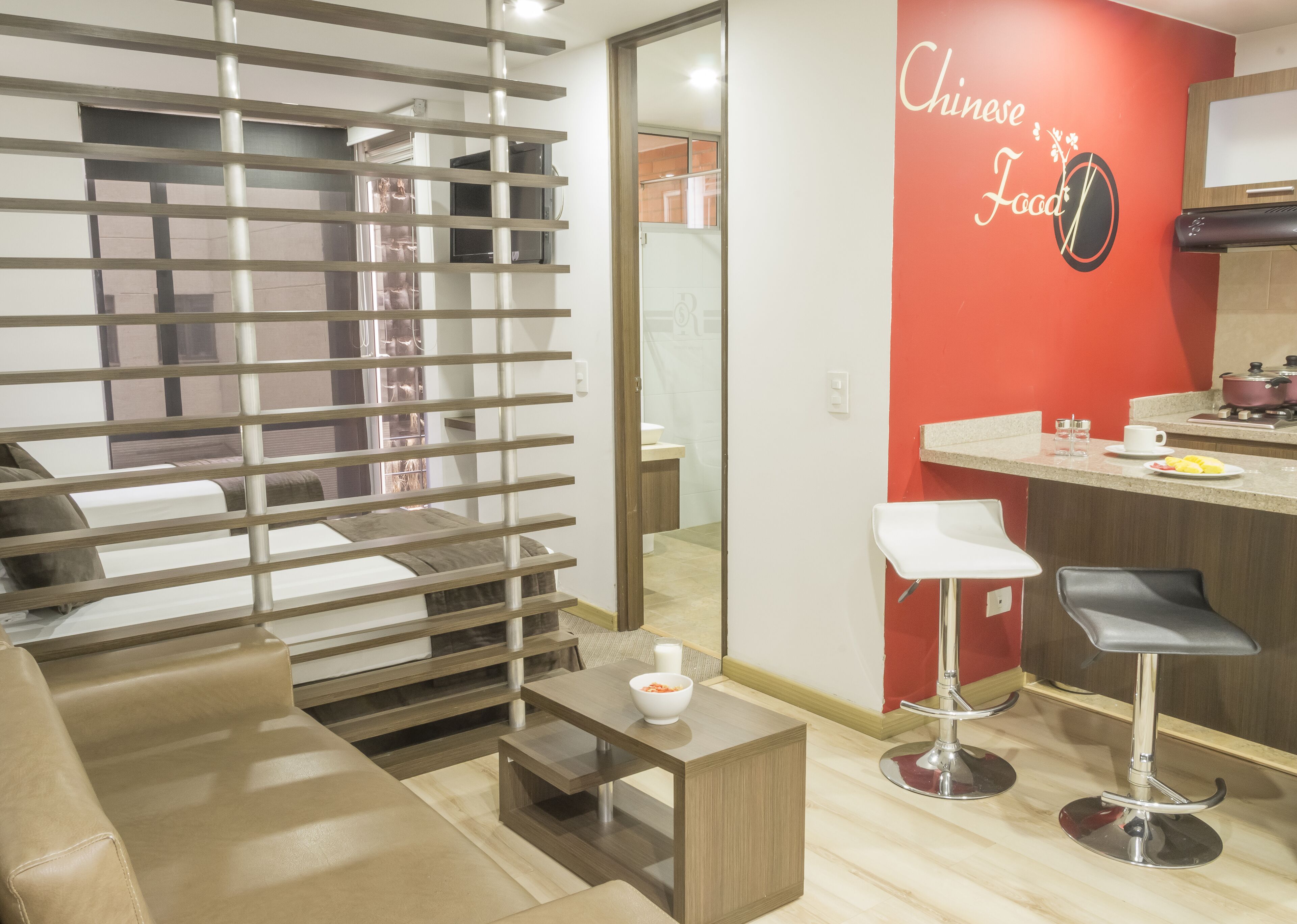 Una sala de estar moderna con un sofá, una mesa de centro y una zona de cocina con una pared roja de acento y un letrero que dice "Chinese Food".