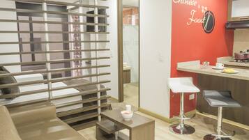Una sala de estar moderna con un sofá, una mesa de centro y una zona de cocina con una pared roja de acento y un letrero que dice "Chinese Food".