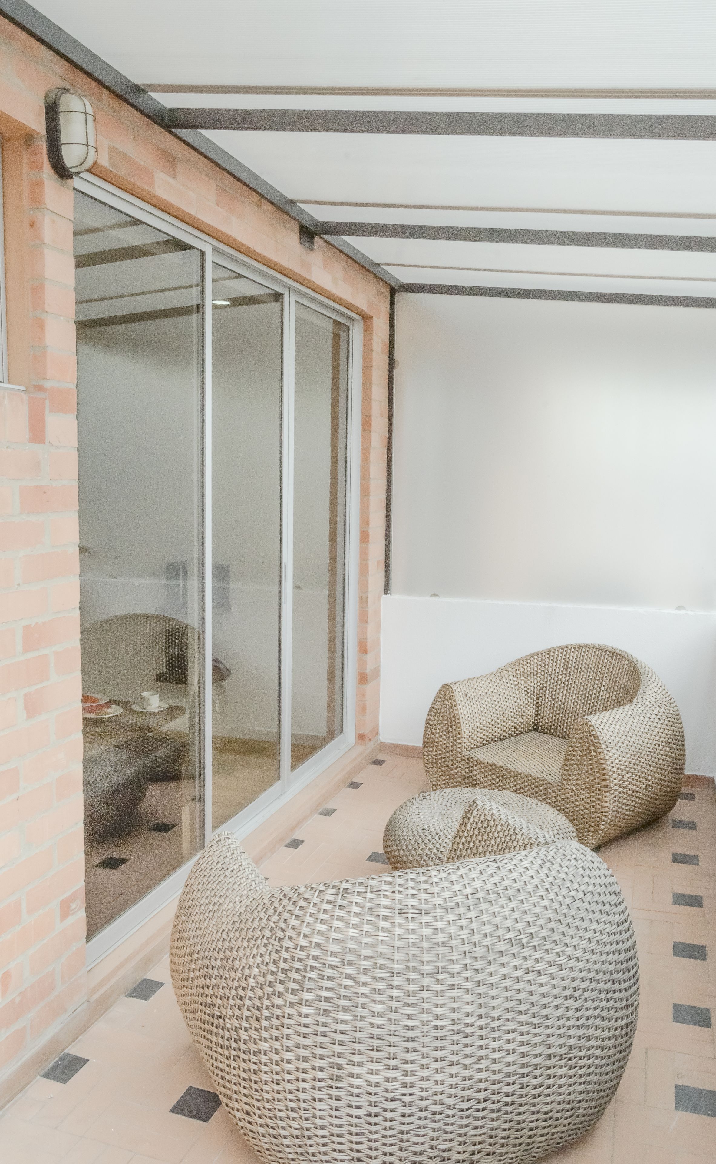 Un espace extérieur moderne, aménagé avec des meubles en osier, une entrée avec une porte vitrée et un sol carrelé.