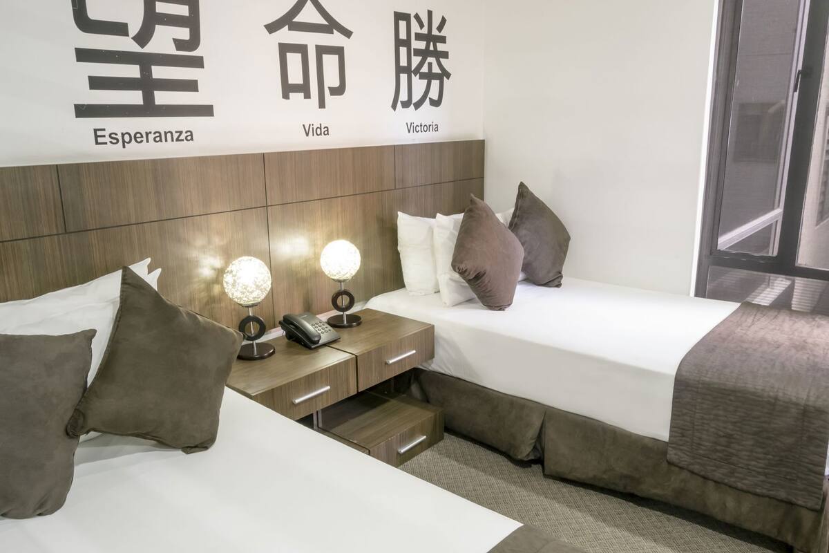 A hotel room with two beds, a wooden headboard, bedside lamps, a phone, and a window.