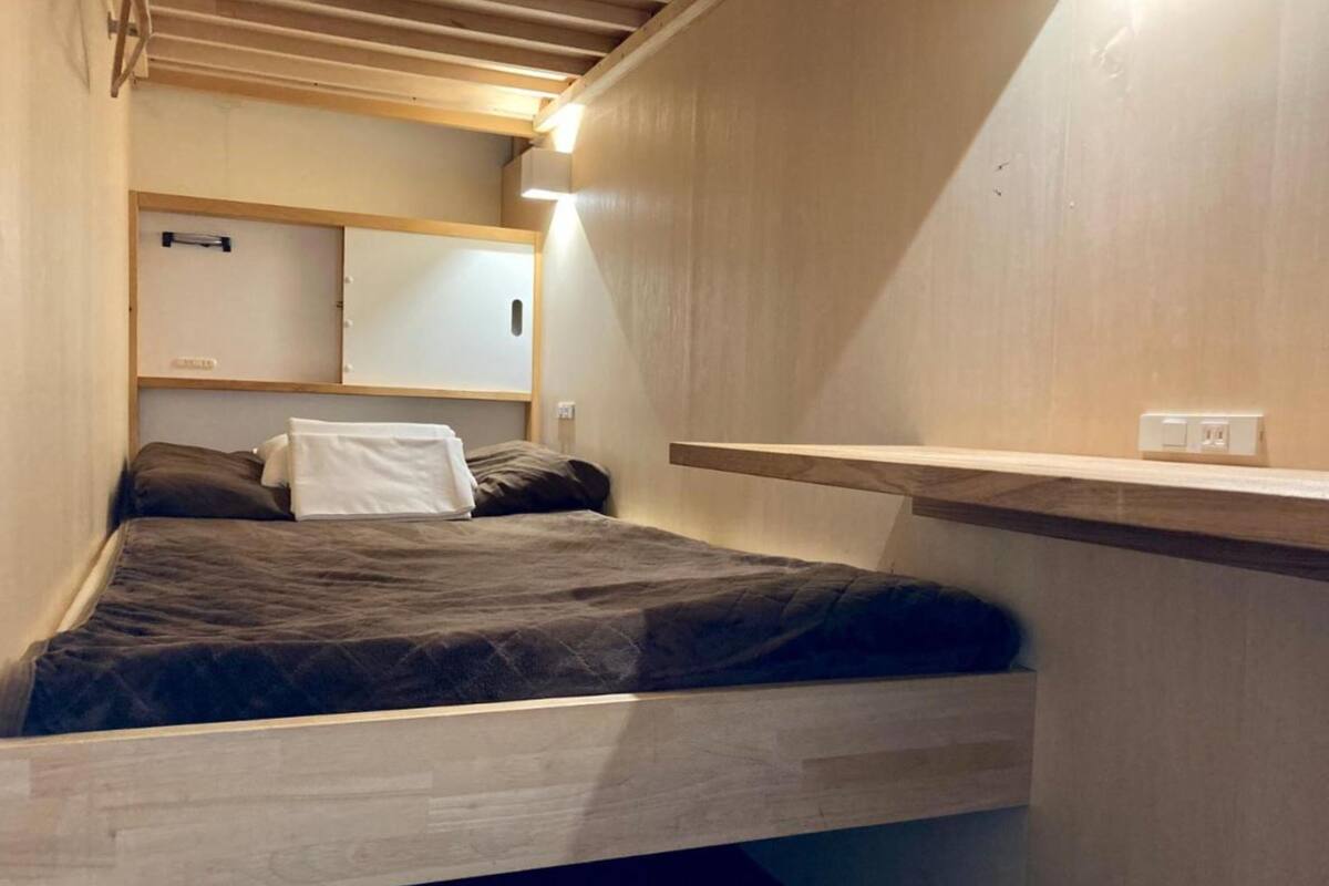 A compact bedroom with a bed, a bedside table, and a wall-mounted shelf.