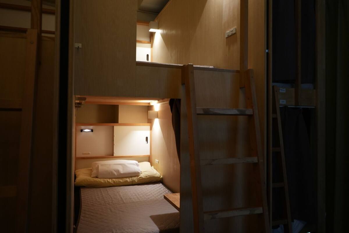 A compact room with a bunk bed, a ladder, and a small desk area.