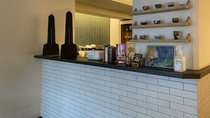 A hotel reception area with a counter, a sign for lost items, a framed picture, and shelves with decorative items. - Santiago Guesthouse Kyoto (Kyoto)
