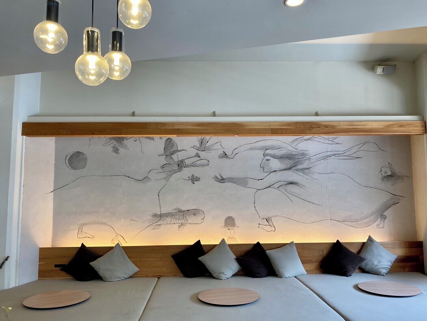 A modern room with a large wall mural, a wooden headboard, and a seating area with cushions and round wooden tables.