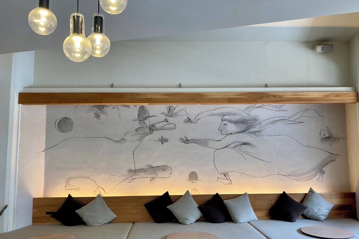A modern room with a large wall mural, a wooden headboard, and a seating area with cushions and round wooden tables.