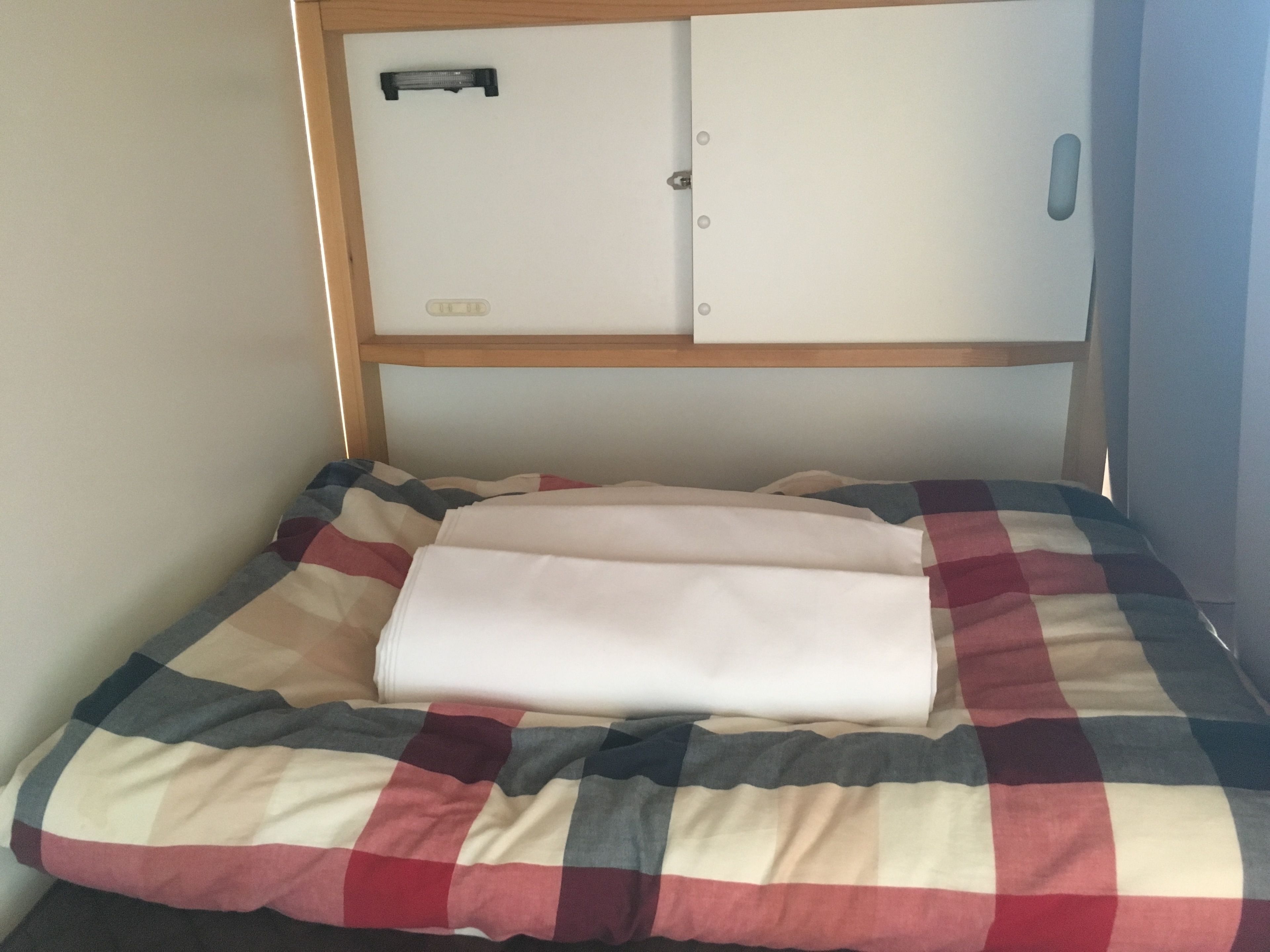 A bed with a checkered bedspread, a folded white blanket, and a headboard with a storage compartment.