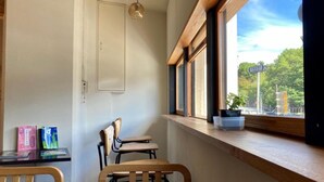 A small, cozy room with a wooden table and chairs, a window with a view of the street, and a door. - Santiago Guesthouse Kyoto (Kyoto)
