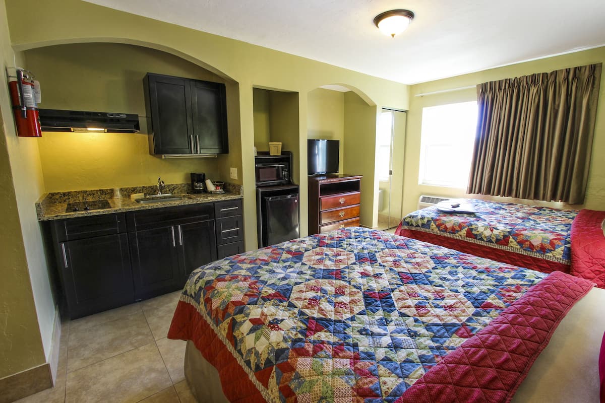 A hotel room with two beds, a kitchenette, a TV, and a window with curtains.