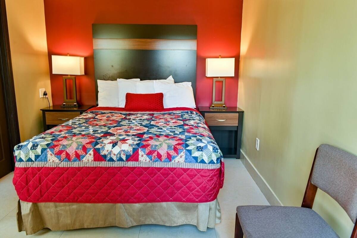 A hotel room with a large bed, two bedside tables with lamps, a wooden headboard, and a chair.