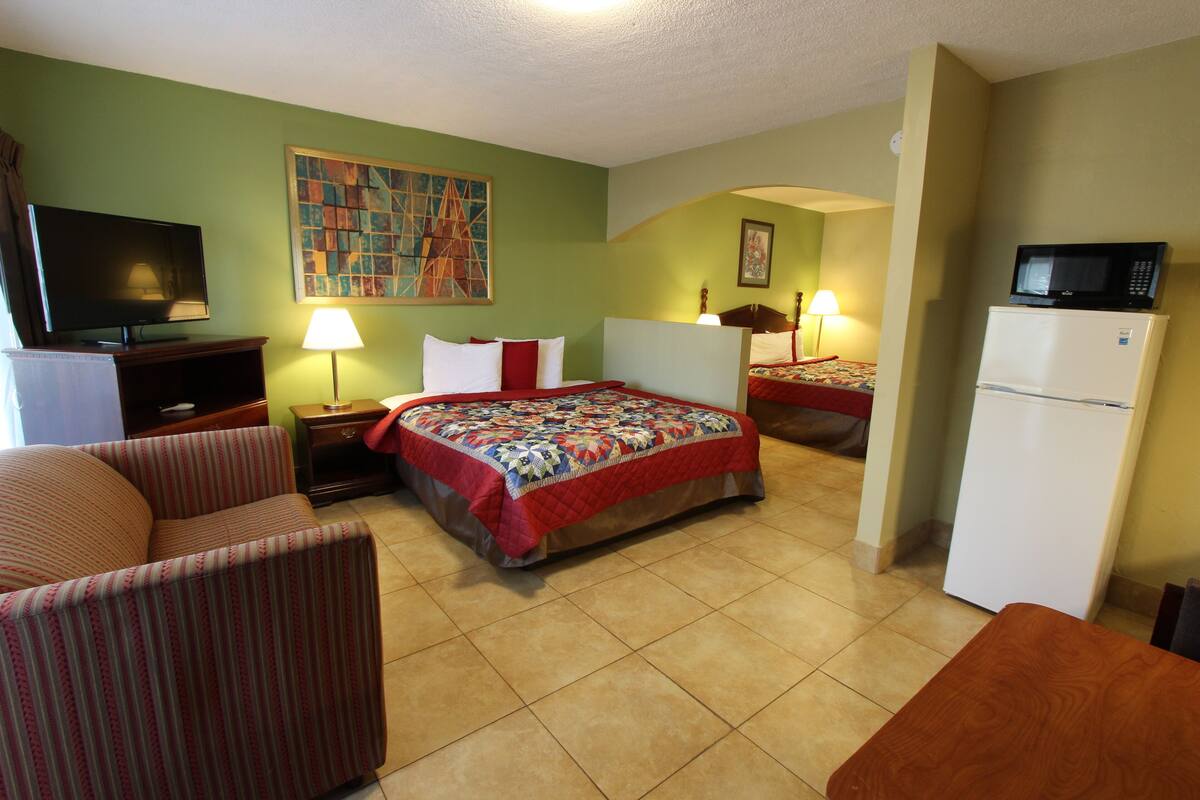 A hotel room with a bed, a TV, a refrigerator, and a chair.
