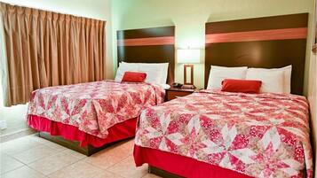 Habitación de hotel con dos camas, cada una con colcha de motivos florales y detalles en rojo. La habitación tiene una pared verde y una cortina marrón.