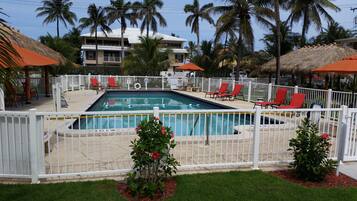 Zona de piscina con piscina cercada, sillas reclinables rojas y palmeras.