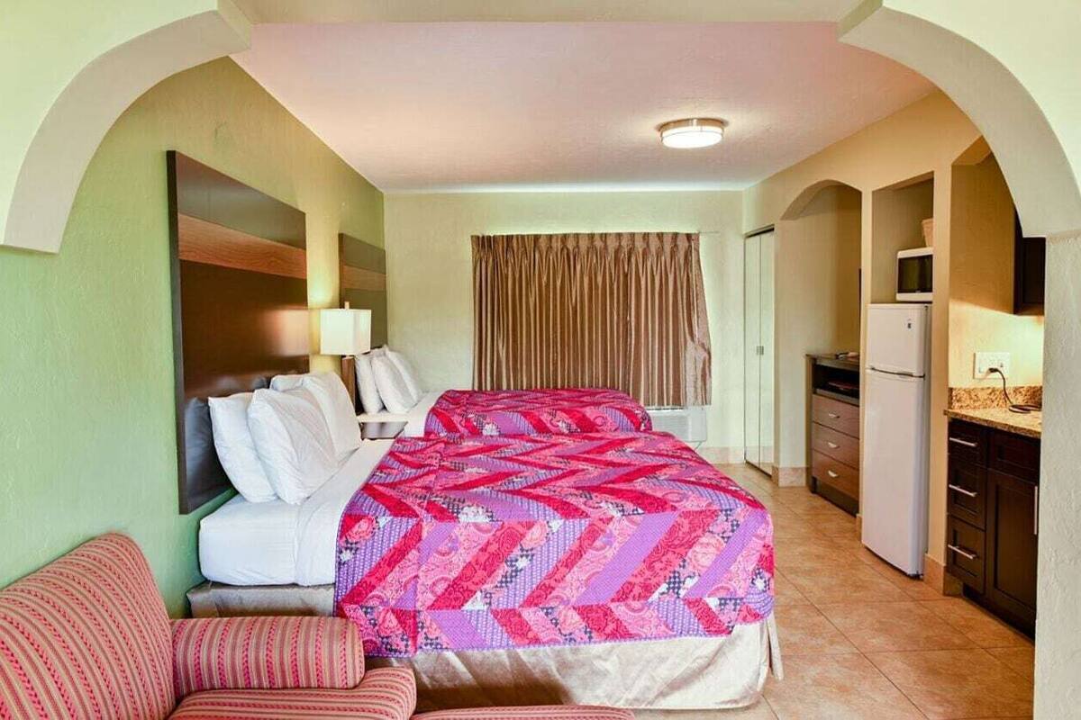 A hotel room with two beds, a kitchenette, and a bathroom.