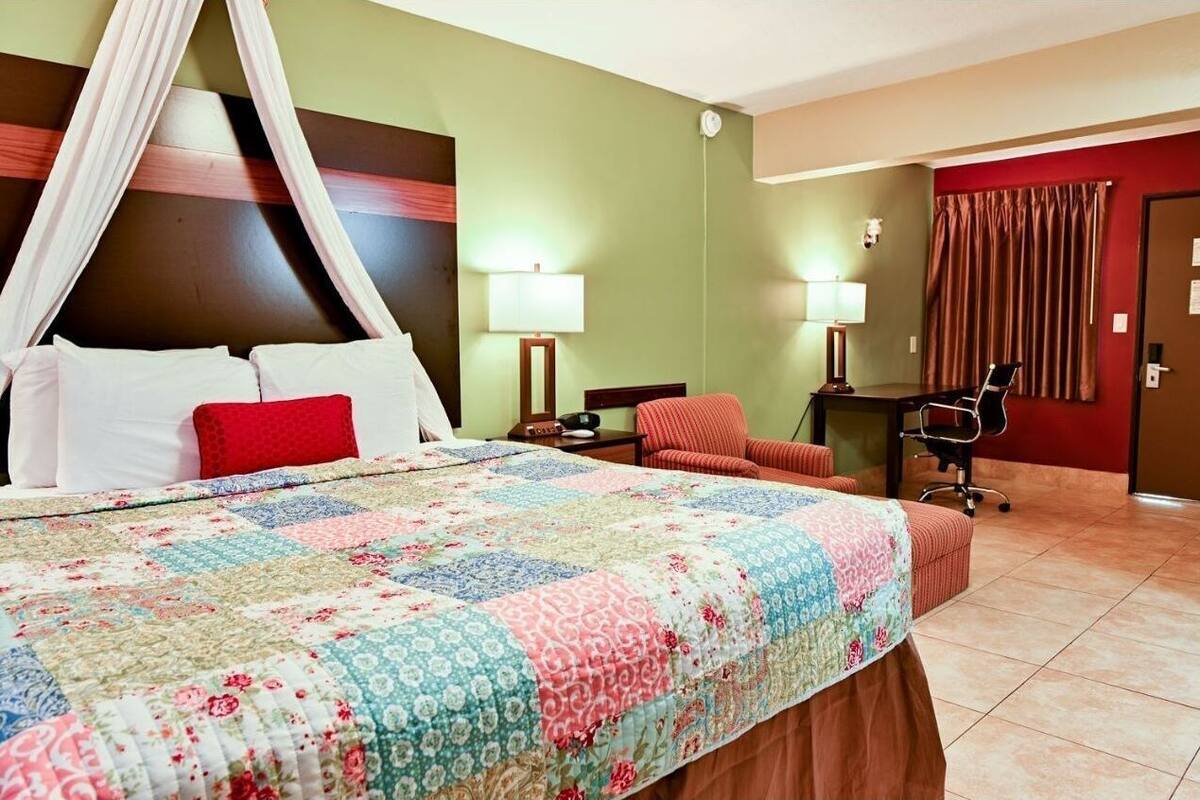 A hotel room with a bed, two bedside tables, a desk, a chair, and a curtain.