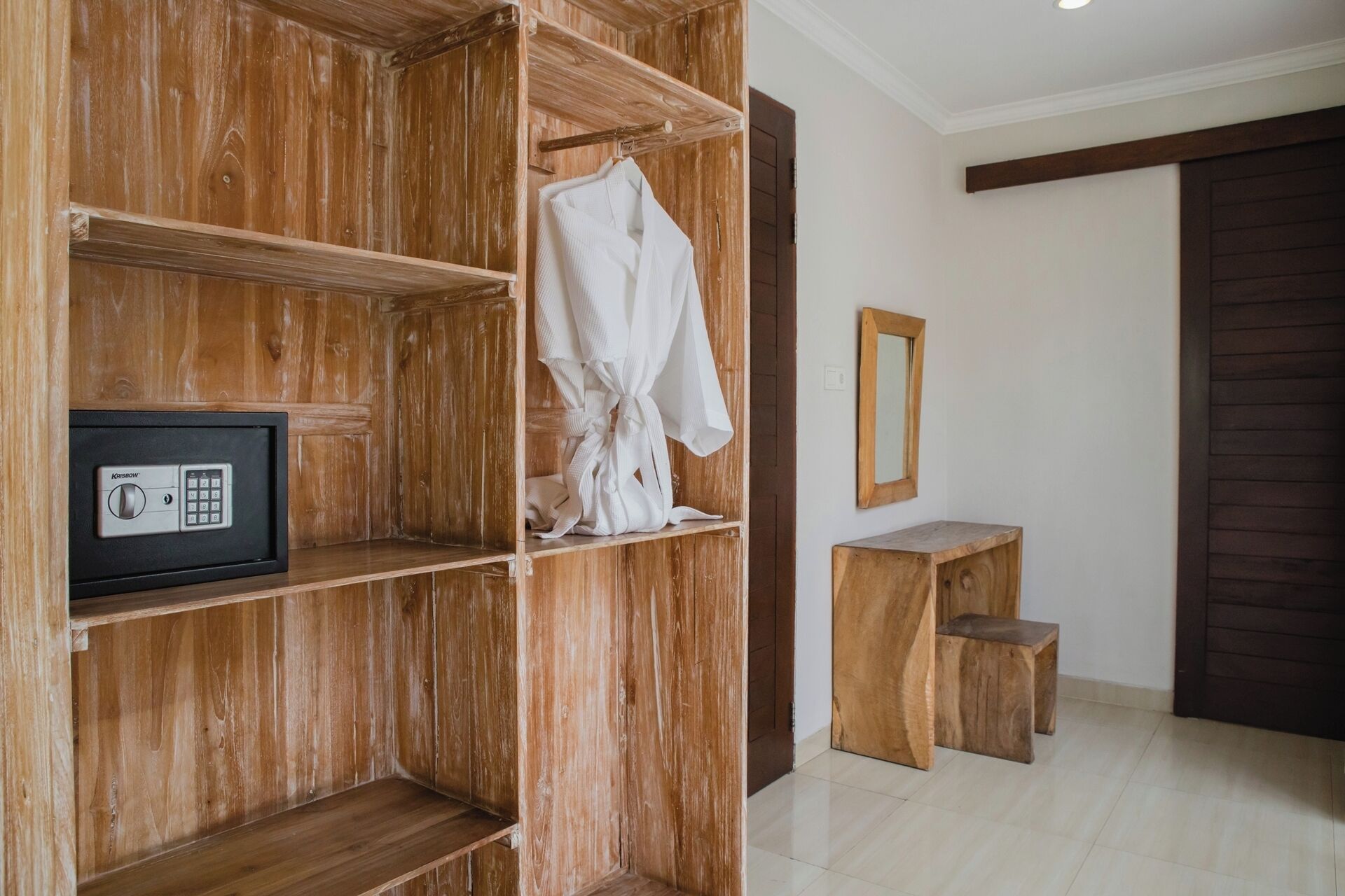 A wooden wardrobe with a built-in safe, a mirror, and a small wooden stool.