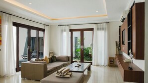 Una sala de estar moderna con un sofá, un reposapiés y una mesa de centro, grandes puertas correderas de vidrio y un televisor montado.