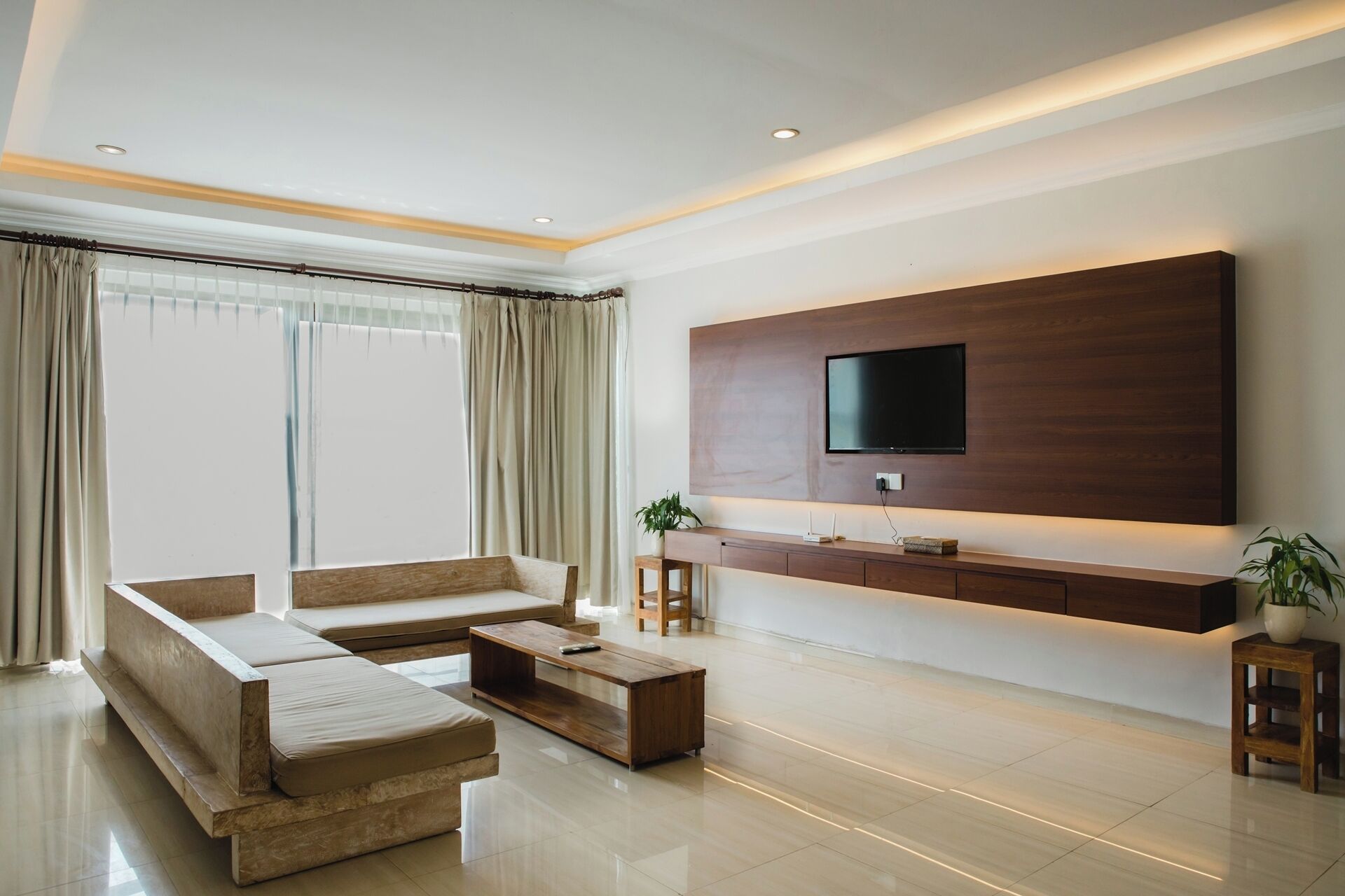 A modern living room with a large flat-screen TV mounted on a wooden wall, a sofa set, a coffee table, and a potted plant.
