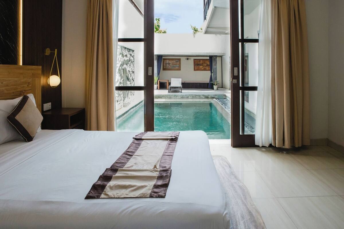 Quarto de hotel com uma cama grande, vista para uma piscina e varanda.