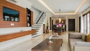 Amplia sala de estar con una mesa de centro de madera, un sofá, una escalera y una cocina al fondo.