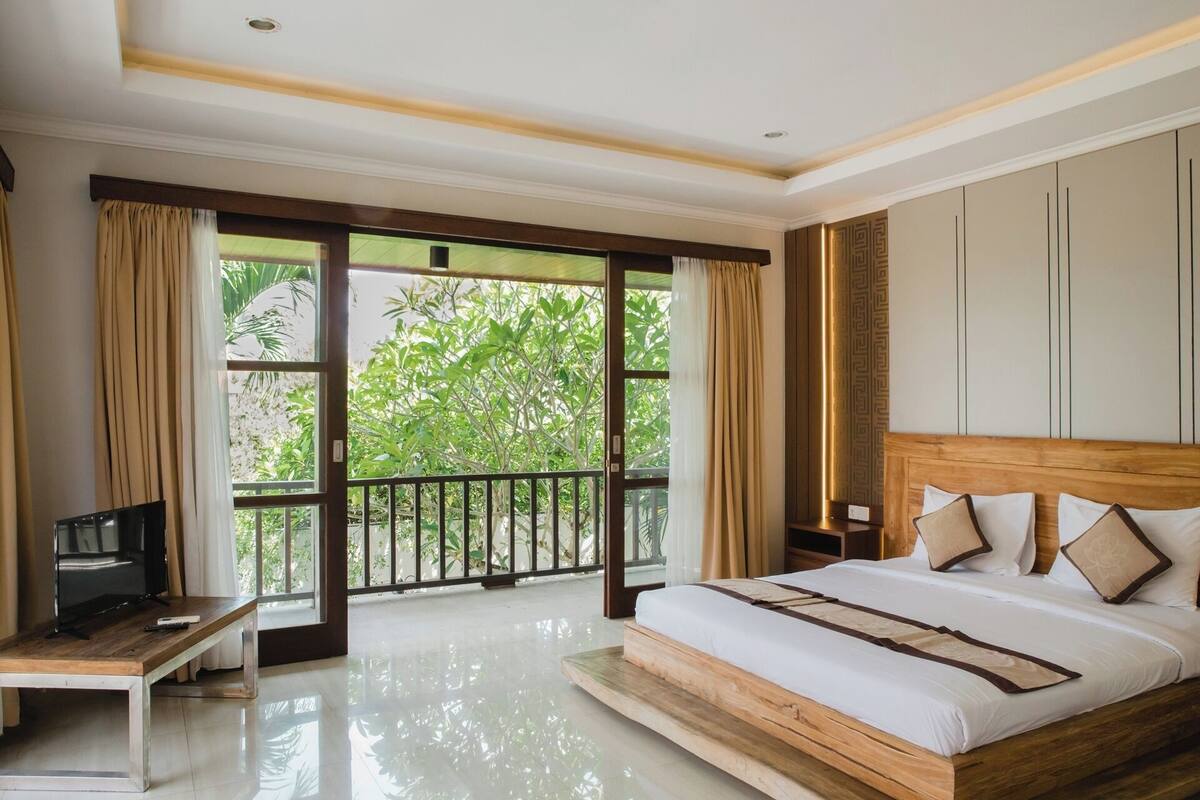 Quarto com uma cama grande, televisão e varanda com cortinas.