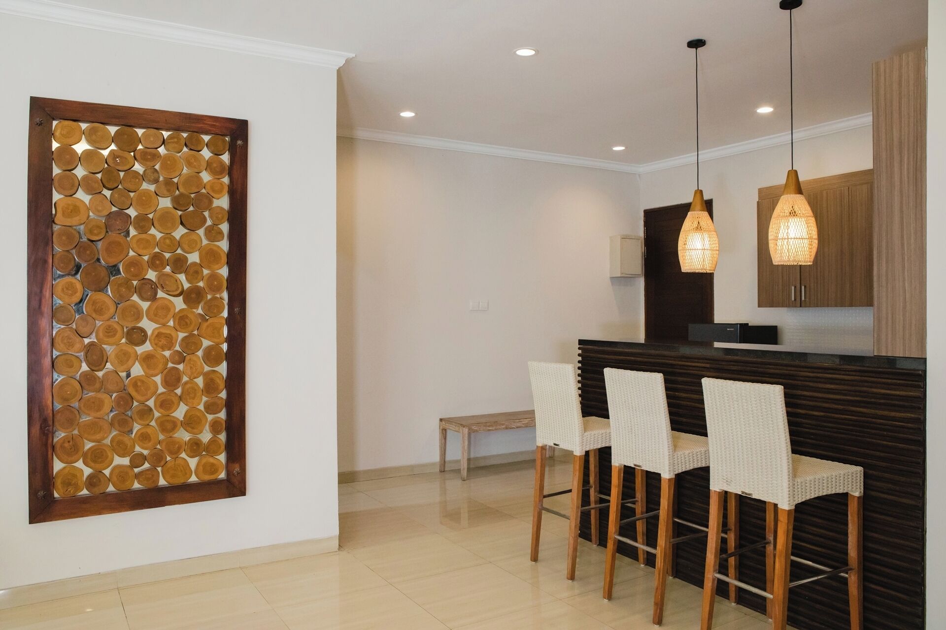 A modern kitchen with a wooden island, three wicker chairs, pendant lights, and a decorative wall panel.