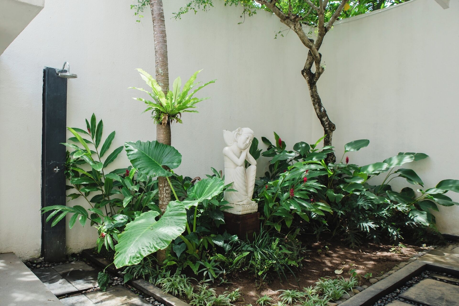 A garden with a statue, various plants, and a concrete pathway.