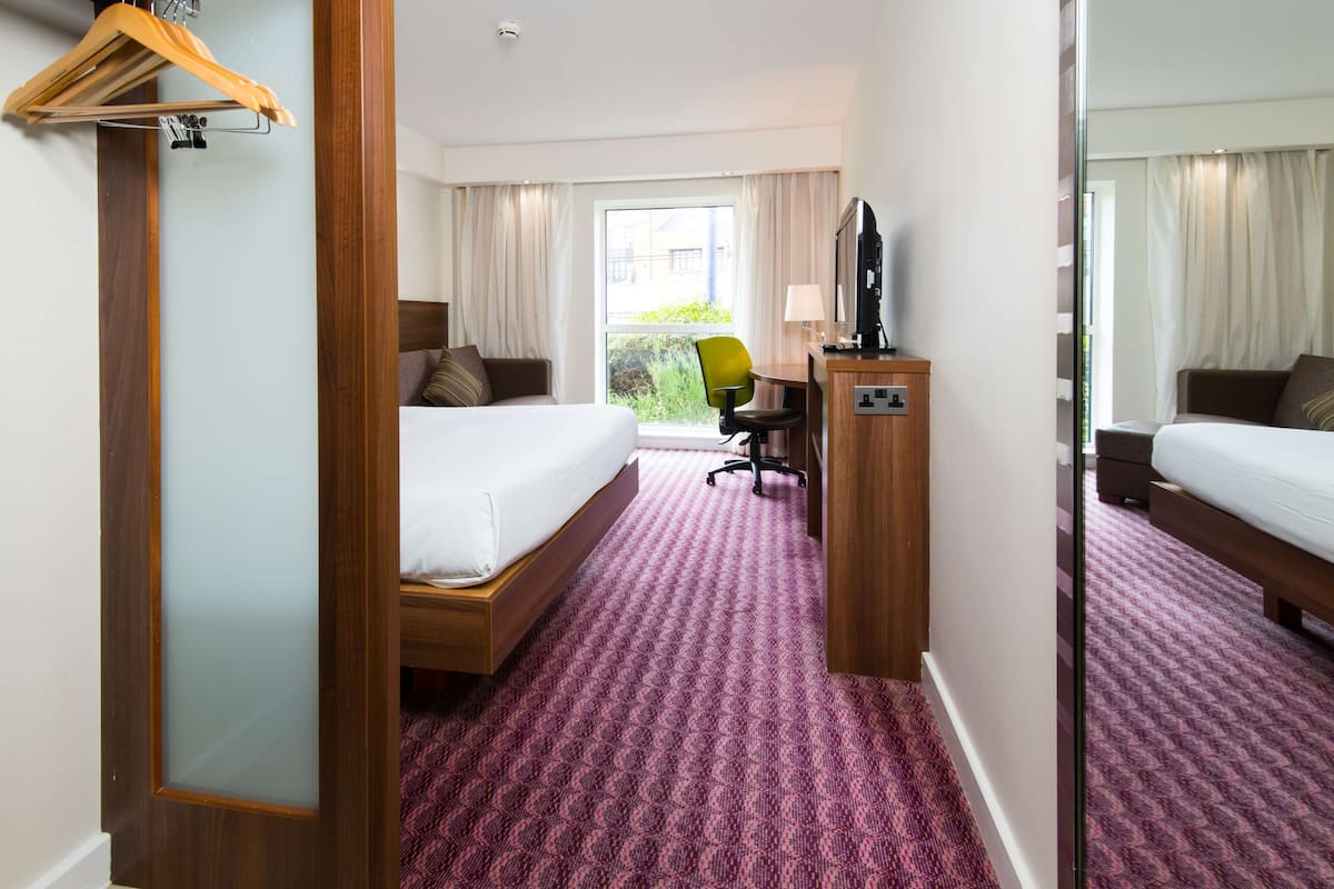 Habitación de hotel con dos camas, un escritorio con silla, un televisor y una ventana con cortinas.