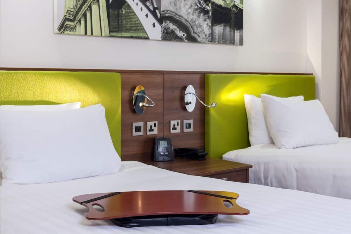 Habitación de hotel con dos camas, una mesita de noche con teléfono, una lámpara de pared y un cuadro sobre las camas.