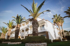 Un hotel de varios pisos con balcones, palmeras y un cielo despejado.