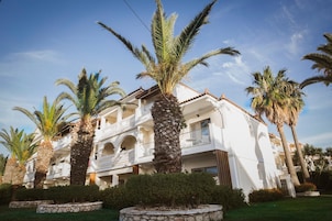 Un hotel de varios pisos con balcones, palmeras y un cielo despejado.