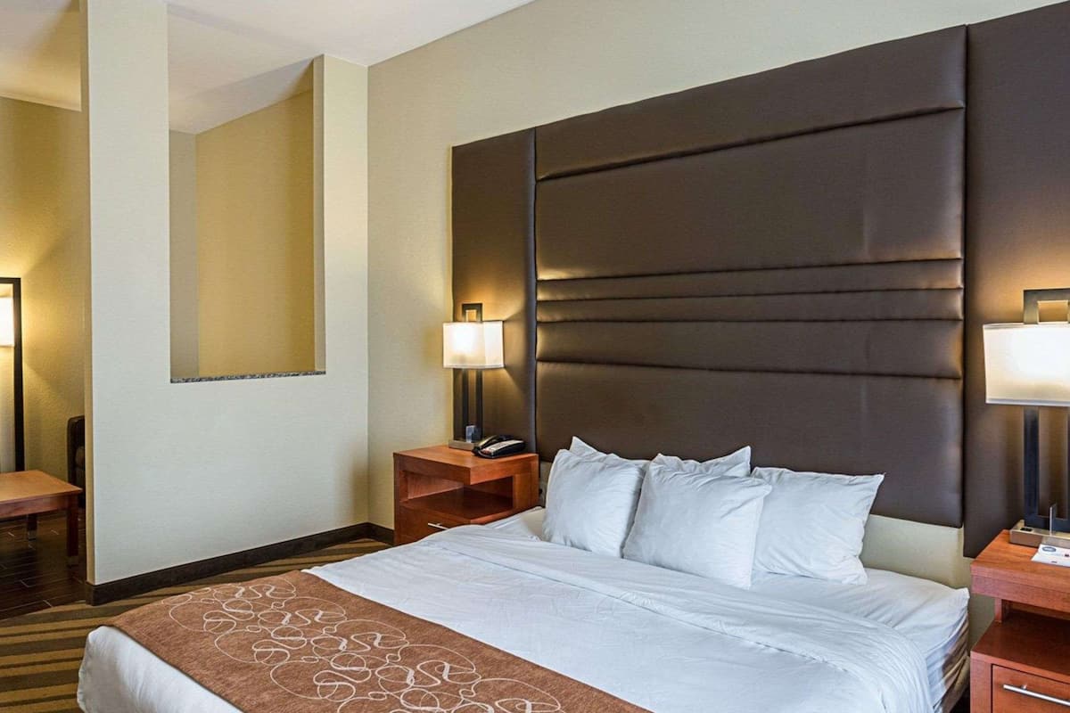 A hotel room with a large bed, two bedside tables, a nightstand, a lamp, and a mirror on the wall.