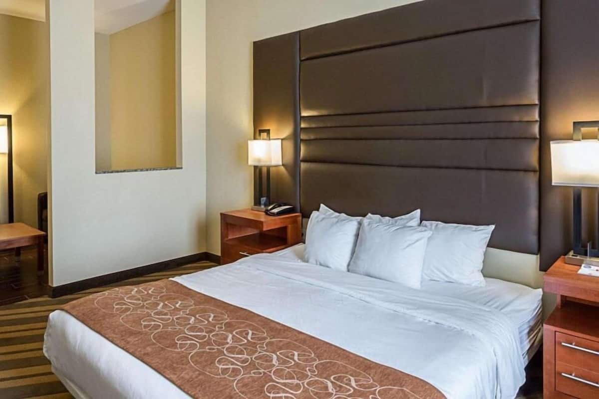 A hotel room with a large bed, two bedside tables, a nightstand, a wall-mounted lamp, and a mirror.