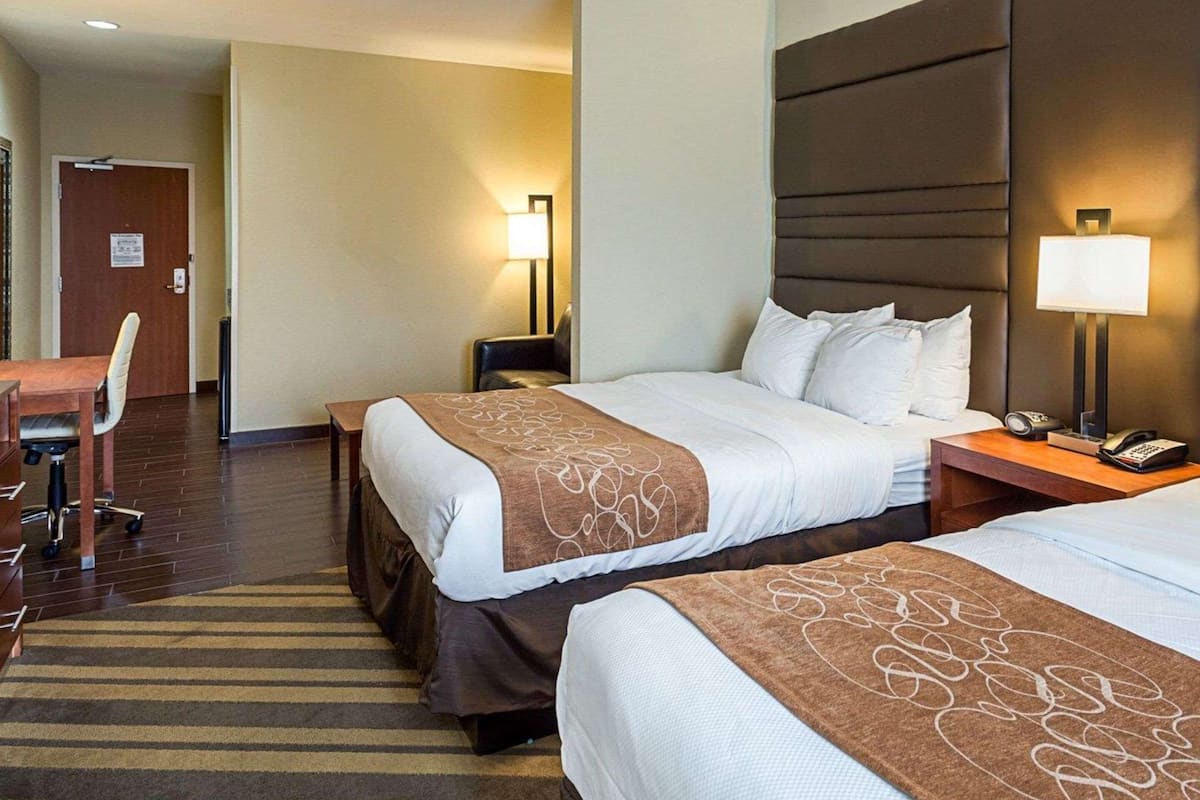 A hotel room with two beds, a desk, and a chair.