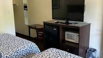 Habitación de hotel con dos camas, un escritorio, televisor, microondas y ventilador de techo.