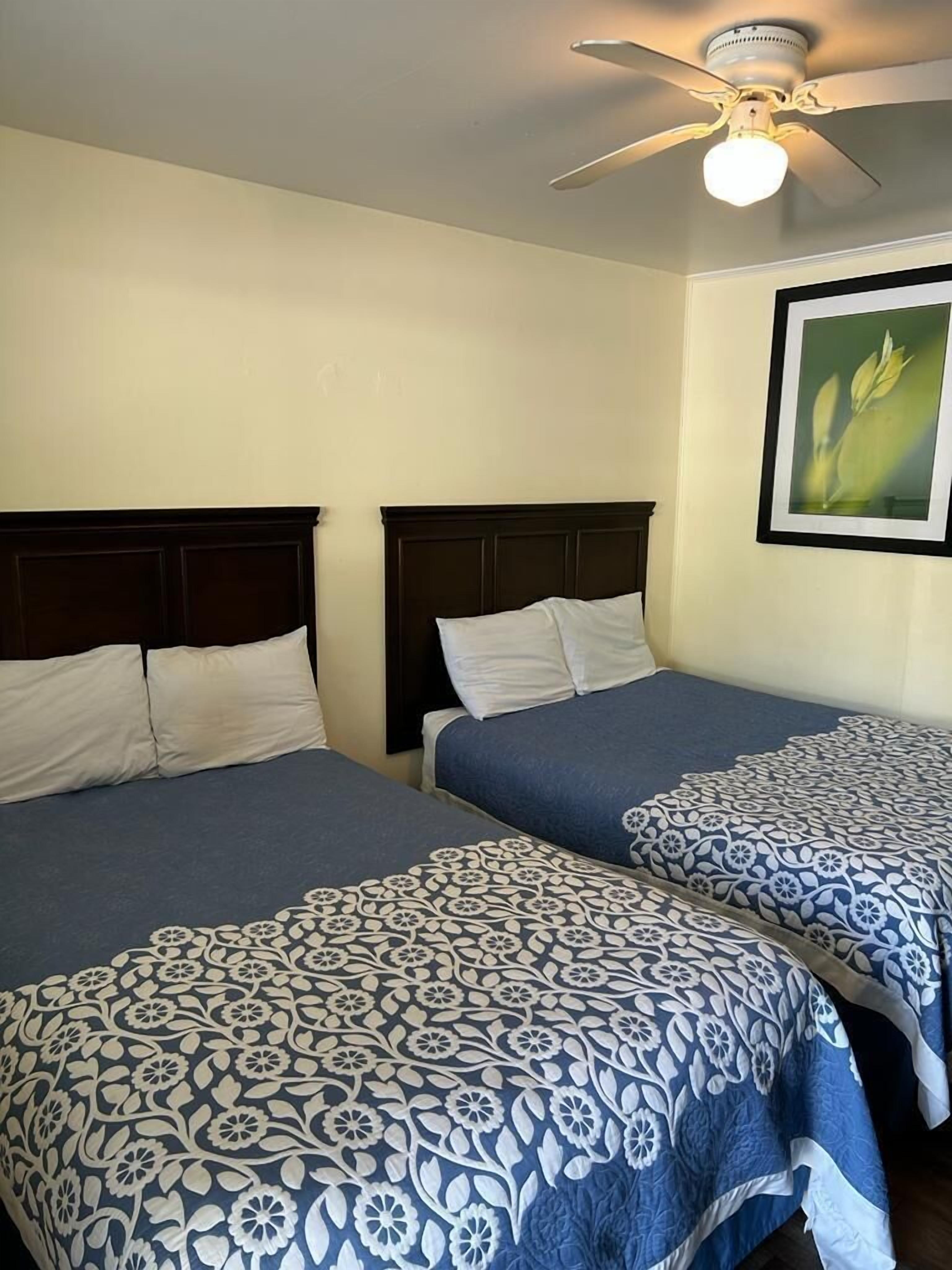 Une chambre d’hôtel avec deux lits, un ventilateur de plafond et un tableau encadré au mur.