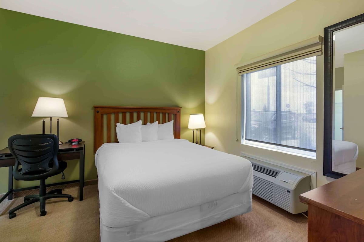 A hotel room with a bed, desk, chair, and a large window.