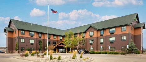 A multi-story hotel with a prominent American flag, a landscaped entrance, and a parking area.
